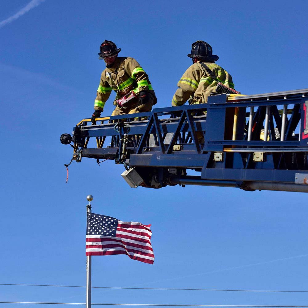 two firefighters on the crane part of the fire truck holding the raptor flood